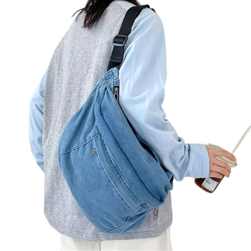 Femme qui porte en bandoulière un grand sac banane en jean bleu clair __switch:Bleu